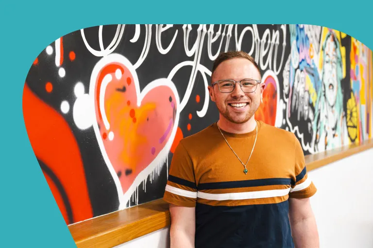 An energetic, casual young professional is smiling in front of a mural