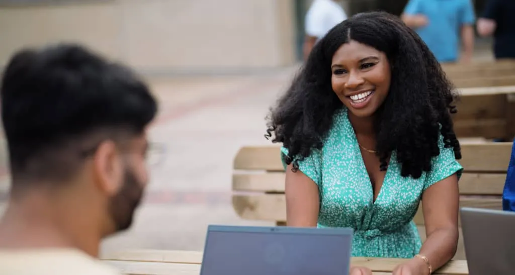 Black woman in green dress smiles whilst talking to a male colleague