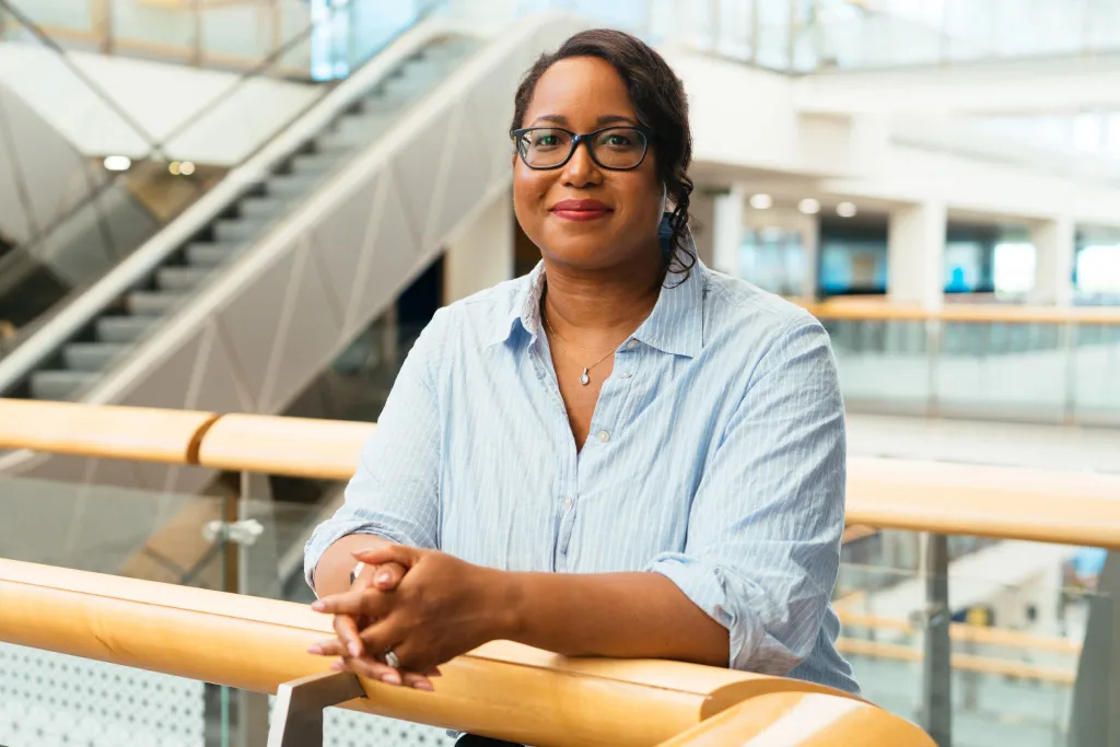 A smiling marketing employee leans on an office railing