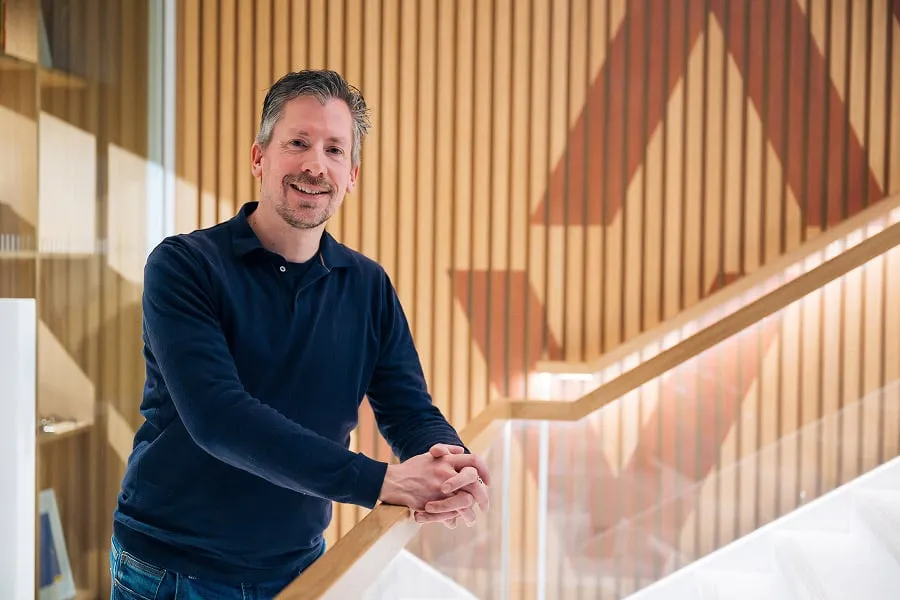 Man With Goatee Beard Wearing Long Sleeved Dark Blue Shirt Stood Against Railing in Office