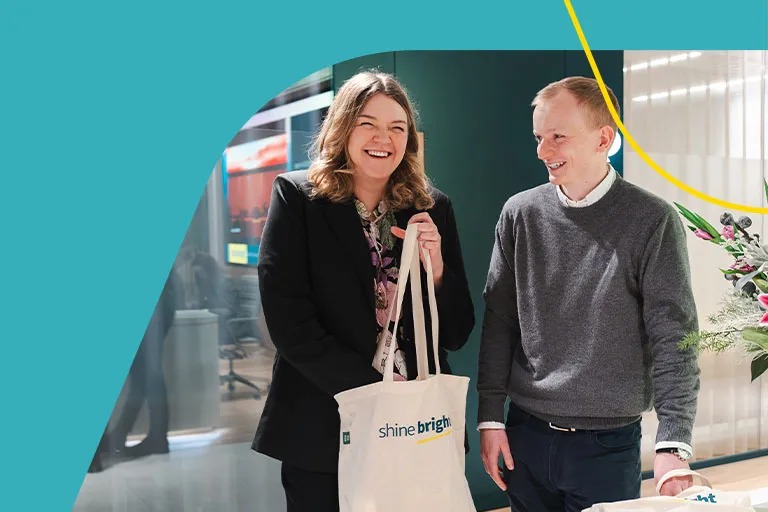 Two people talking, holding an Aviva Shine Bright tote bag