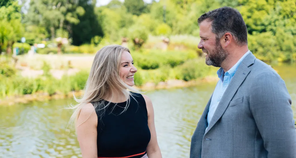 Two finance colleagues laugh outside by a body of water in a park