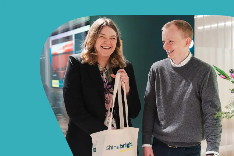 Two people talking, holding an Aviva Shine Bright tote bag