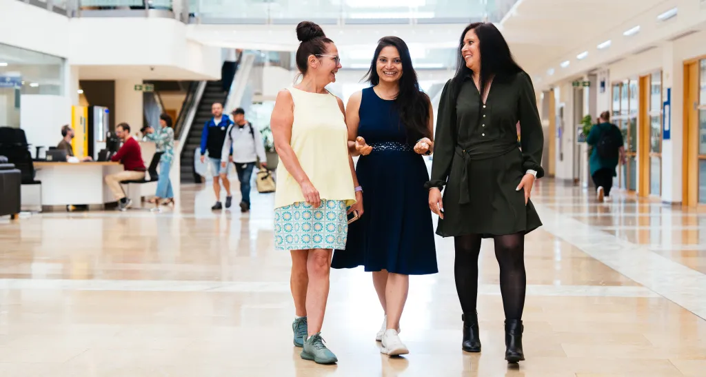 Three female digital colleagues walk and talk in an vibrant office foyer