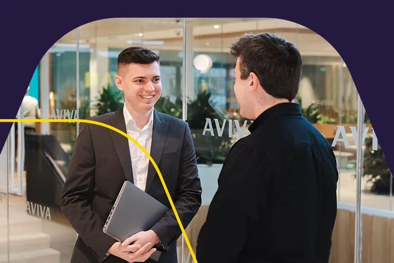 A professional man in a suit talks to a colleague with an Aviva meeting room in the background