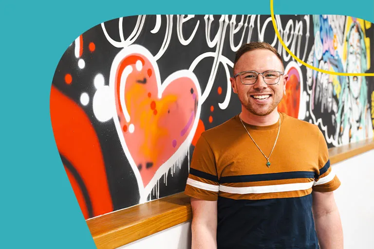 An energetic, casual young professional is smiling in front of a mural