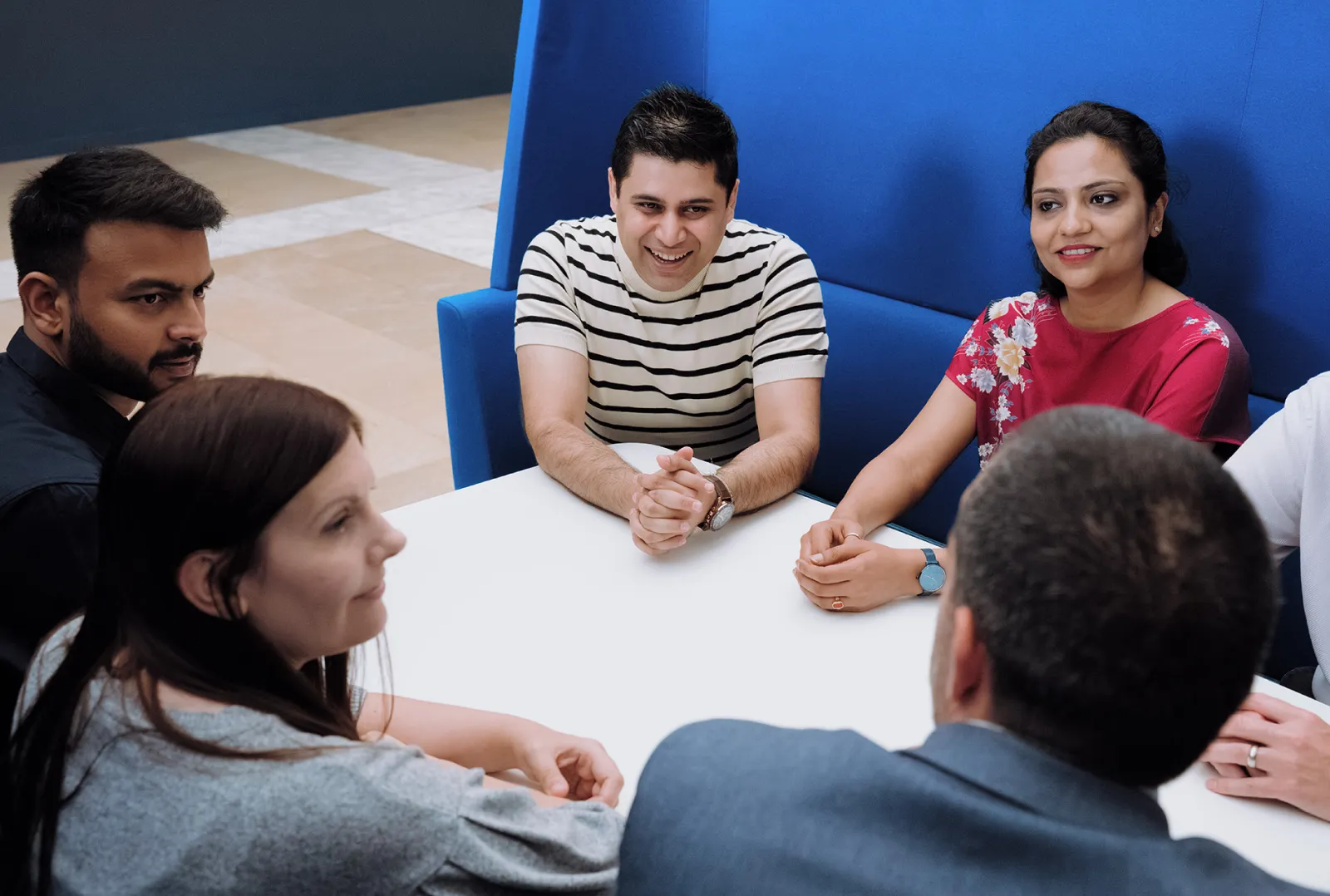 A group of DLG Legal Services colleagues enjoy a conversation sitting around a sociable table space.