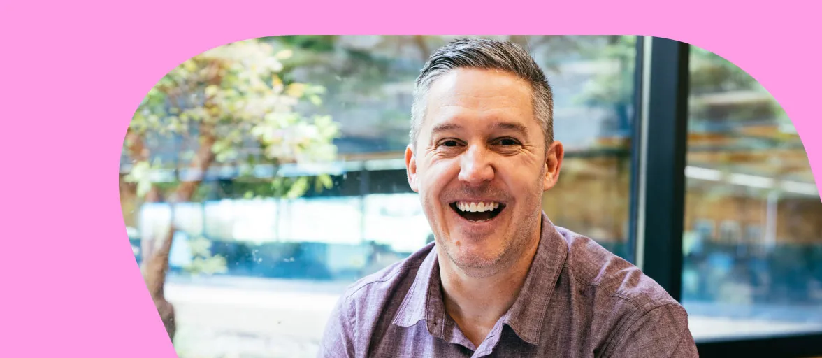 A male software developer smiles widely by a window