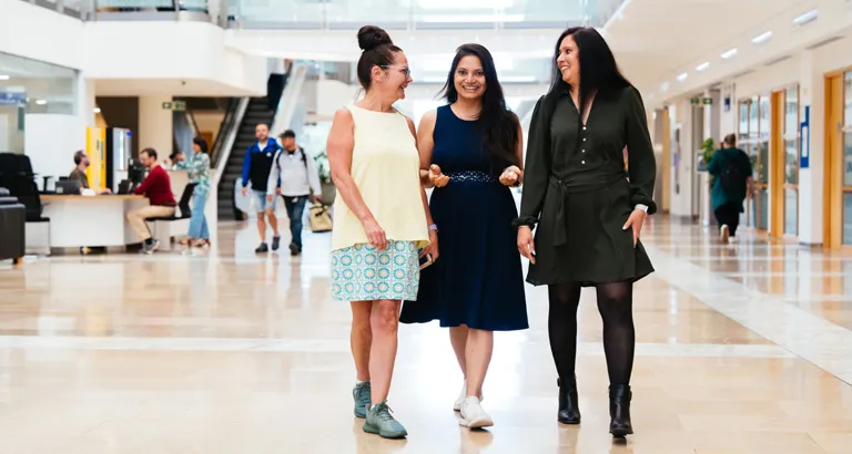 Three female digital colleagues walk and talk in an vibrant office foyer