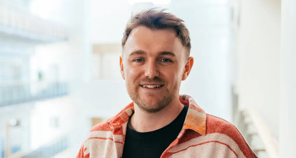 A tech worker smiles straight on to camera on an upper level of the office