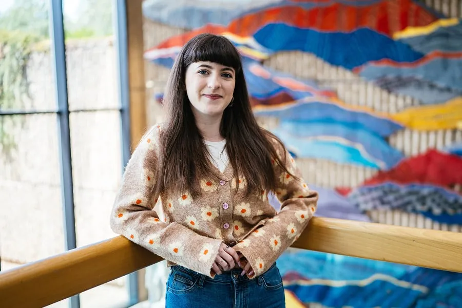 Smiling Woman With Fringe and Flower Patterned Cardigan Leaning Against Railing