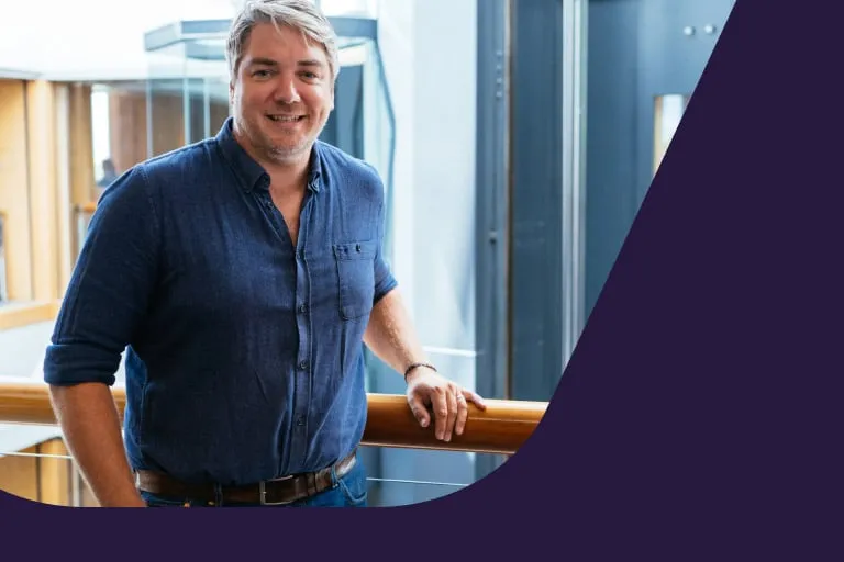 Smiling Middle Aged Man Wearing Blue Button up Shirt Stood Against Railing